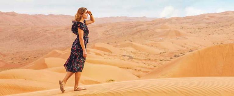 Nainen kävelee hiekka-aavikolla.